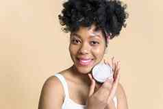有机化妆品概念微笑非洲美国女人持有Jar奶油米色背景相机