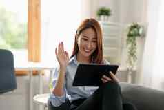图像快乐亚洲女人微笑挥舞着手数字平板电脑说话聊天视频调用首页