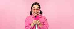 肖像亚洲女孩太阳镜智能手机女人移动电话浏览应用程序站粉红色的背景