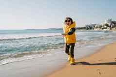 男孩黄色的橡胶靴子玩沙子海滩学校孩子触碰水秋天冬天海孩子有趣的运行波海岸春天假期假期概念