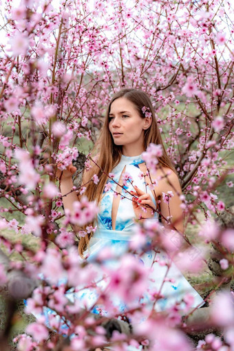 年轻的美丽的女人蓝色的衣服长头发享受开花<strong>桃子树</strong>
