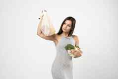 快乐年轻的女人持有字符串可重用的网袋有机蔬菜积极的女站绿色工作室背景生态友好的购物