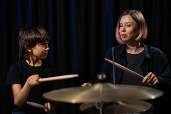 年轻的高加索人女人教男孩玩鼓工作室黑色的背景音乐学校学生