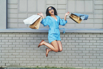 购物使女孩<strong>飞跃</strong>快乐完整的长度拍摄有吸引力的年轻的女人跳快乐持有购物袋砖墙