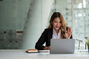 肖像微笑亚洲女人挥舞着会说话的视频<strong>调用</strong>成功的年轻的女人坐着白色西装业务会议移动PC