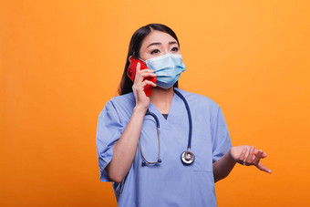 年轻的成人亚洲护士穿口罩听诊器会说话的智能手机病人