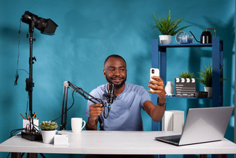 视频博客坐着视频博客工作室持有麦克风采取自拍智能手机