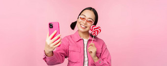 肖像时尚的快乐亚洲女孩采取自拍糖果萝莉波普糖果微笑采取照片移动应用程序站粉红色的背景