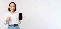 热情的年轻的亚洲女人指出手指智能手机屏幕显示广告移动电话白色背景