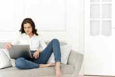 年轻的积极的女人移动PC检查新闻互联网坐着沙发工作远程