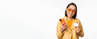 在线购物交付概念快乐朝鲜文女孩时尚的衣服持有信贷卡智能<strong>手机</strong>笑微笑站白色背景
