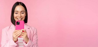图像微笑亚洲企业女人西装看智能手机应用程序移动电话应用程序站粉红色的背景