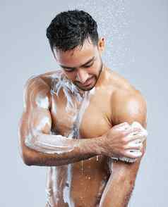 泡沫擦洗工作室拍摄英俊的年轻的男人。采取淋浴灰色背景