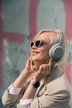 肖像金发女郎女人耳机听音乐太阳镜模型穿时尚的无线耳机享受听很酷的音乐