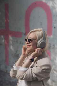 肖像金发女郎女人耳机听音乐太阳镜模型穿时尚的无线耳机享受听很酷的音乐