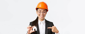 特写镜头微笑亚洲女工程师架构师头盔业务西装持有首页微型指出手指小房子工作建筑建设白色背景
