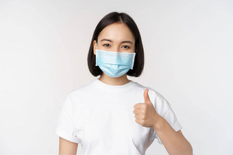 微笑亚洲女孩医疗面具显示拇指批准好赞美赞美公司站白色背景