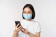 健康科维德概念年轻的亚洲女人医疗面具移动电话打字智能手机站白色背景