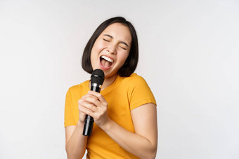 快乐亚洲女孩跳舞唱歌<strong>卡拉ok</strong>持有麦克风手有趣的站白色背景