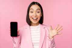 惊讶热情的亚洲女商人显示移动电话屏幕智能手机应用程序接口站粉红色的背景