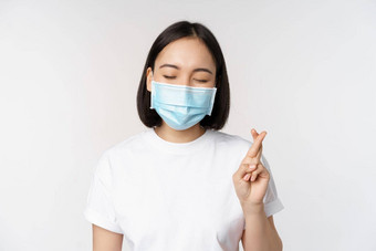 科维德医疗保健医疗概念图像亚洲女孩医疗脸面具交叉手指祈祷使微笑站白色背景