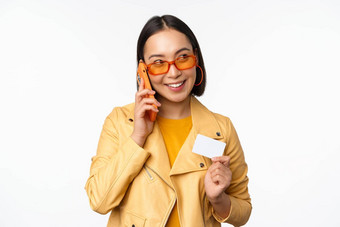时尚的亚洲女模型会说话的智能<strong>手机</strong>显示信贷卡站白色背景