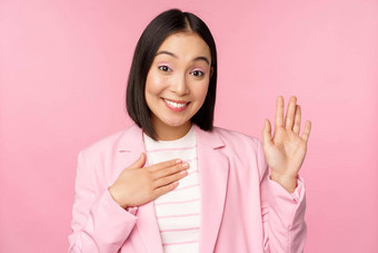 肖像可爱的亚洲女商人提高手介绍办公室微笑卖弄风情的站粉红色的背景西装