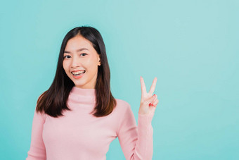 年轻的亚洲美丽的女人微笑穿硅胶矫正家臣牙齿显示地摆胜利手指