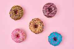类型色彩斑斓的甜甜圈装饰洒糖衣柔和的粉红色的背景
