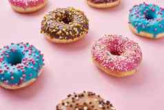 模式类型色彩斑斓的甜甜圈装饰洒糖衣柔和的粉红色的背景前视图平躺