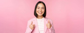 专业女商人亚洲企业女人显示拇指微笑赞美赞美站西装粉红色的背景