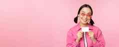 肖像时尚的现代亚洲女孩显示折扣信贷卡很高兴支付非接触式概念购物站粉红色的背景