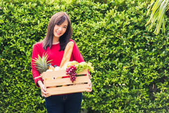 女人农民站持有完整的新鲜的食物生蔬菜水果木盒子