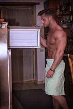 英俊的肌肉发达的男人。厨房内部冰箱