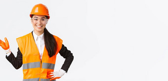 微笑快乐的亚洲女建设经理介绍优秀企业投资者穿安全眼镜头盔手套指出手左骄傲白色背景