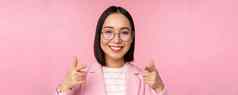 祝贺你微笑亚洲企业女人首席执行官经理西装眼镜指出手指相机招聘赞美赞美站粉红色的背景