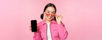肖像时尚的现代亚洲女孩显示移动电话屏幕智能<strong>手机</strong>应用程序接口站太阳镜粉红色的背景