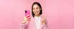 时尚的亚洲女商人女孩西装采取自拍智能手机视频闲谈，聊天移动电话应用程序摆姿势粉红色的工作室背景