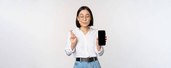 充满希望的年轻的亚洲女人显示移动电话屏幕应用程序接口手指交叉希望smth使支付站白色背景
