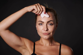 工作室拍摄有吸引力的高加索人女人按摩脸<strong>刮痧</strong>沙玉石头按摩器美水疗中心皮肤护理概念