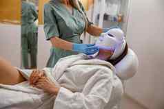 女人化妆品过程领导面部面具光子治疗