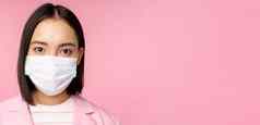关闭肖像日本女商人医疗脸面具西装相机站粉红色的背景