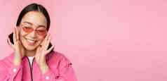 关闭时尚的朝鲜文女孩太阳镜微笑快乐摆姿势粉红色的背景人脸概念