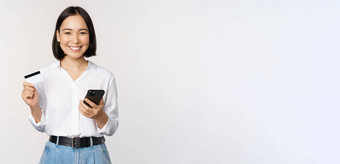 在线购物概念图像年轻的亚洲现代女人持有信贷卡智能手机购买智能手机应用程序支付<strong>非接触</strong>式站白色背景