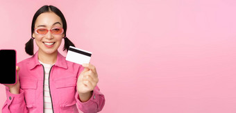 图像微笑朝鲜文女人显示信贷卡移动电话屏幕智能<strong>手机</strong>应用程序接口支付在线购物非接触式站粉红色的背景