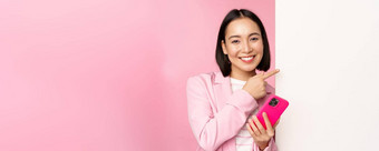 <strong>图</strong>像微笑亚洲企业女人西装持有智能手机指出董事会显示<strong>图</strong>表信息标志空白色墙站粉红色的背景