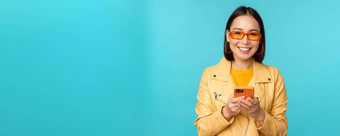 微笑亚洲女孩太阳镜智能手机应用程序持有移动电话站蓝色的背景
