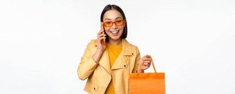 现代朝鲜文女孩购物持有商店袋会说话的移动电话微笑站白色背景