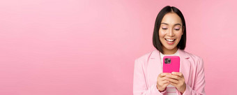 肖像亚洲女孩西装智能手机微笑快乐站粉红色的工作室背景