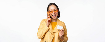 时尚的亚洲女模型会说话的智能手机显示信贷卡站白色背景